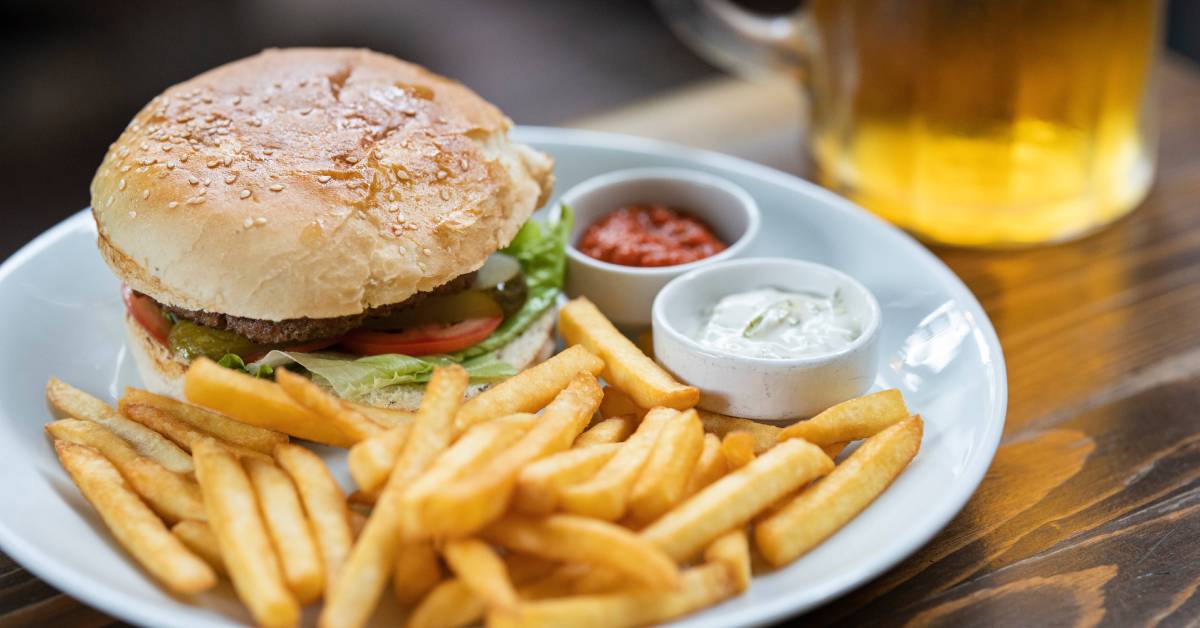 Burger-with-fries-and-dipping-sauce-on-a-plate-beside-a-glass-of-beer