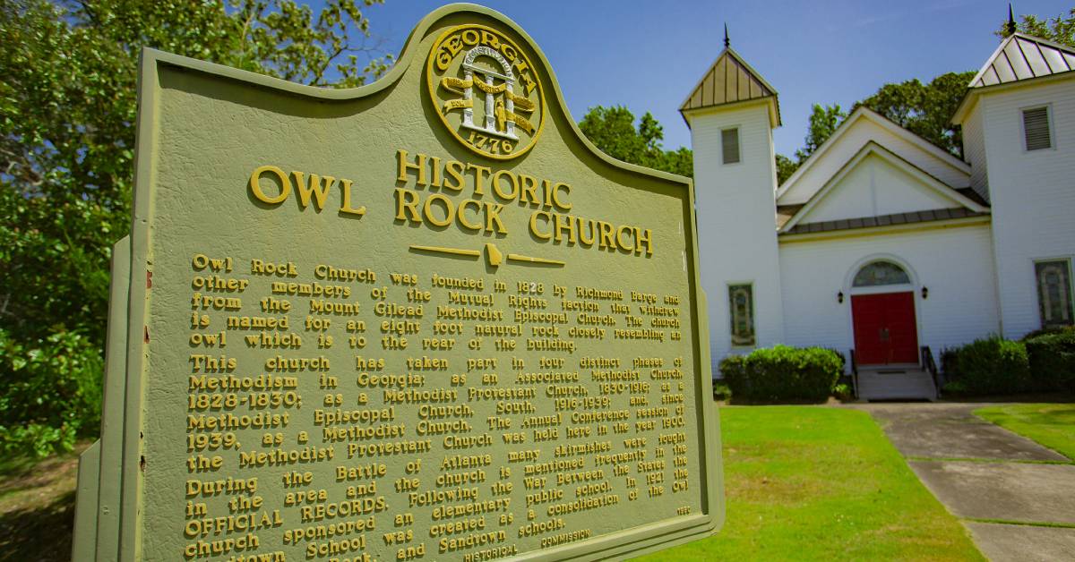 Historical-marker-for-_Owl-Rock-Church_-in-front-of-a-white-church-with-a-red-door-under-a-blue-sky