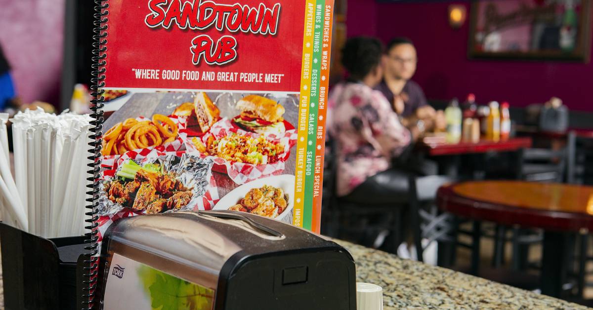 Menu-of-a-pub-featuring-food-images-with-a-napkin-dispenser-in-front-and-tables-in-the-background